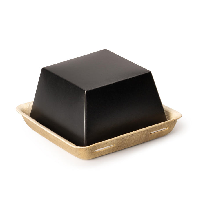 Zweiteilige, quadratische Take-away-Box aus Kraftpapier. Die beige Bodenplatte aus Palmblatt mit erhöhtem Rand dient als Basis, auf die eine obere, schwarze Kraftpapier-Box festgesteckt wird, 17 x 17 x 8 cm